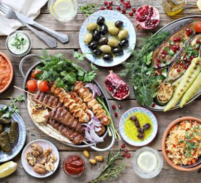Middle eastern, arabic or mediterranean dinner table with grilled lamb kebab, chicken skewers  with roasted vegetables and appetizers variety serving on rustic outdoor table. Overhead view.
